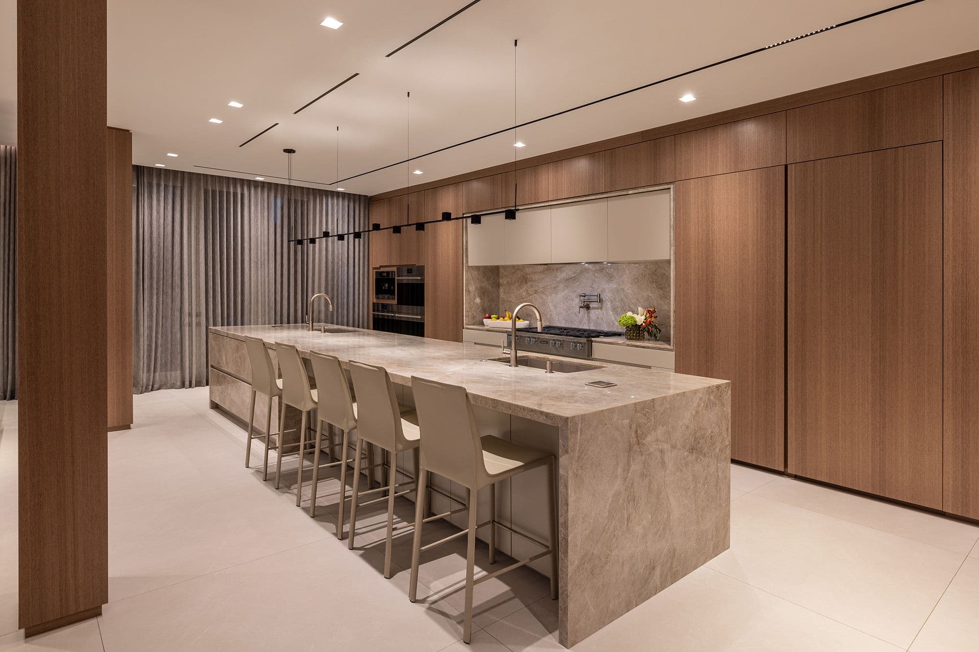 Luxury modern kitchen design featuring a large waterfall island wrapped in heavily veined grey marble with integrated dual sinks and gold faucets.